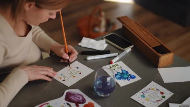Ciężarna Kobieta Maluje Wielkanocną Kartkę Farbami Akwarelowymi Siedząc Przy Stole — Wideo stockowe