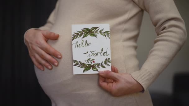 慢动作特写 一个无法辨认的孕妇站在室内拿着生日卡片用手揉肚子的特征 — 图库视频影像