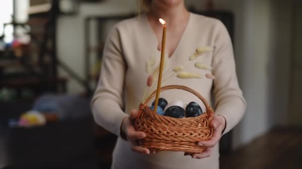 一个孕妇手里拿着一个复活节篮子 手里拿着燃烧的蜡蜡烛和复活节彩蛋 站在公寓的客厅里 一个女人把篮子伸向摄像机 — 图库视频影像
