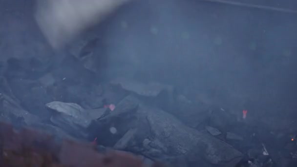 クローズアップ グリルの火はプラスチック製のバーベキューハンドファンで覆われています バーベキューグリルからの煙 バーベキューを無視する過程 グリルの準備 — ストック動画