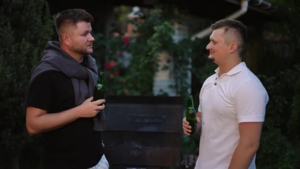ビールを手に開いた2人の男性の会話は 夏の夕方に屋外で立っていました 男性はビールボトルを飲み飲みます — ストック動画