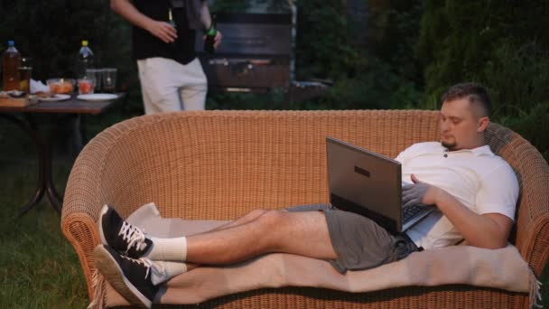 Mężczyzna Leży Wiklinowej Sofie Pracuje Laptopie Letni Wieczór Świeżym Powietrzu — Wideo stockowe