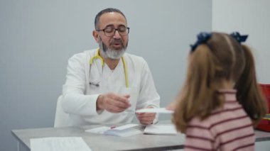 Randevuyu bitirdikten sonra, erkek çocuk doktoru küçük kıza kağıt bir belge verir, sonra beşlik çakar ve çocuğa sarılır.