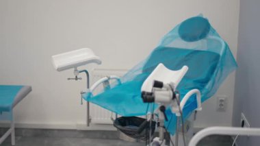 Kliniğin içinde tek kullanımlık mavi çarşafla kaplı jinekolojik bir sandalye var.