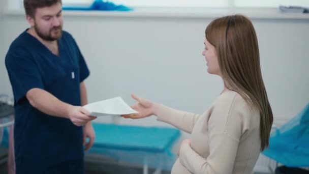 男性医師は妊娠中の患者に保険契約を渡し 笑顔で辞めました 妊娠中の女性は紙片を取り 医師の手を振り向いてオフィスを離れた — ストック動画