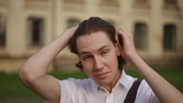 Крупный План Молодой Улыбающийся Парень Смотрит Камеру Выпрямляет Волосы Голове — стоковое видео
