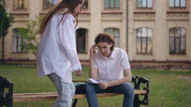 Enstitü binasının yanındaki bankta oturan bir adam sınav görevini çözüyor. Adamın elinde kalem ve dizlerinde açık bir defter var. Bir kız, erkeğin yanına oturur ve görevi tartışırlar.