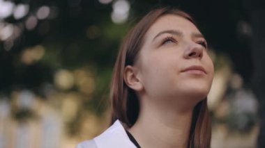 Yakın plan. Bir yaz günü şehir parkında otururken gökyüzüne bakıp hayaller kuran genç bir kızın yüzü.