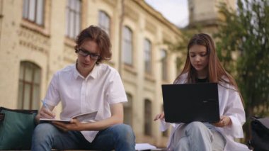 Ağır çekim. Sınavlara hazırlanan öğrenciler, enstitü binasının yanındaki bankta oturuyorlar. Kucağında dizüstü bilgisayarla oturan kız ve elinde cep telefonu olan adam.