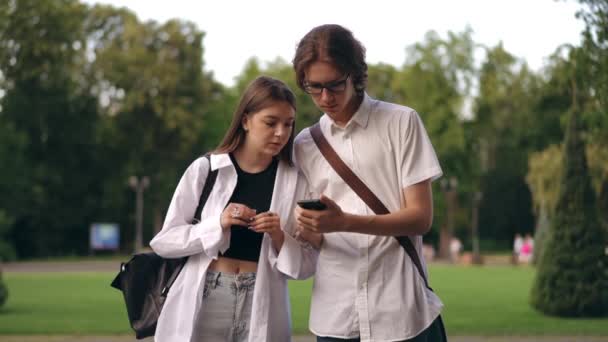 一个男的和一个女的正在看一个手机的屏幕 他手里拿着手机 站在一个夏天的一天 在研究所的公园里 在屏幕上看到了必要的信息 — 图库视频影像