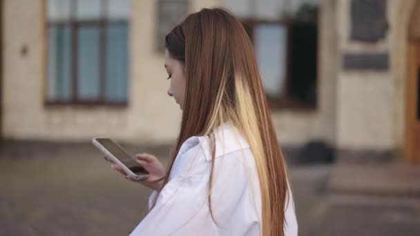 Zwolnij Trochę Dziewczyna Idzie Wzdłuż Budynku Patrzy Ekran Telefonu Komórkowego — Wideo stockowe