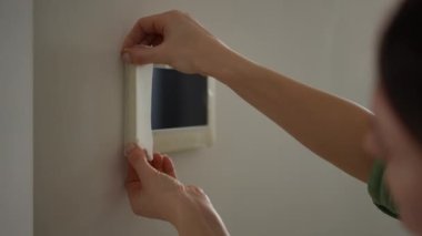 Yakın plan. Bir kadın duvarları boyamadan önce evinin koridorunda duran bir video interkom görüntüsünü maskeleyici bant ile dikkatlice kapatıyor. Bir oda numarası çiz