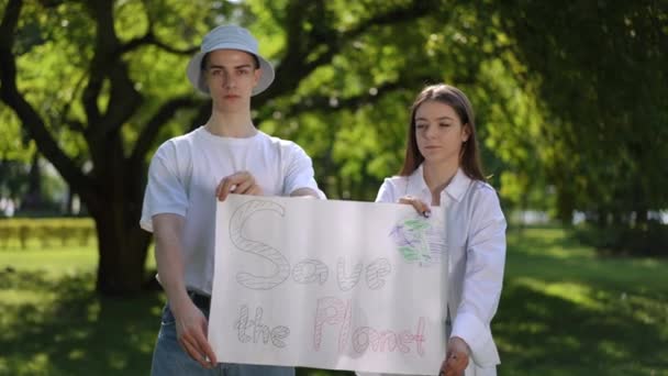惑星を救った 夏の日に公園の屋外での自然保護のための行動 男と女の子はカメラを見てポスターを手に持っている — ストック動画