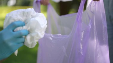 Ağır çekim. Yakın plan. Mavi kauçuk eldivenli bir adam çöpü plastik bir torbaya koyuyor ve o torba tanınmayan bir kızın elinde tutuluyor. Bir yaz gününde şehir parkındaki çöpleri temizlemek.