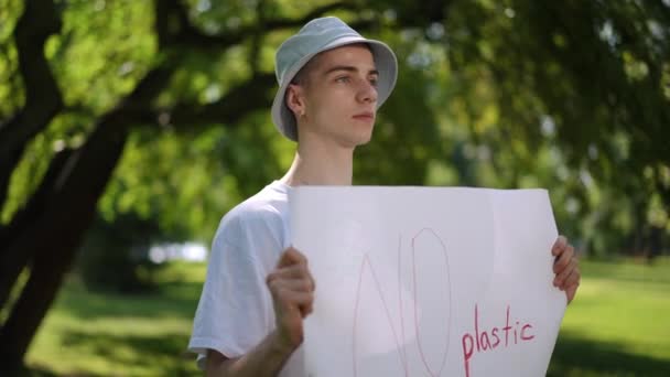 プロテスタントはプラスチックにノーと言う 太陽の帽子をかぶった男は 市の公園の屋外で夏の日に動かずに立って 彼の手にはプラスチック製のポスターを持っていません — ストック動画