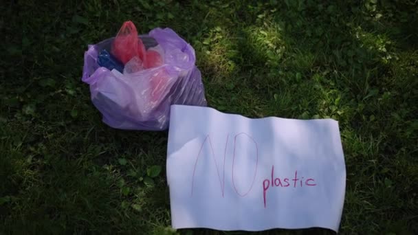 クローズアップ 緑の草の日陰には ゴミ袋とプラスチックなしの言葉のポスターがあります 市立公園でゴミを掃除する — ストック動画