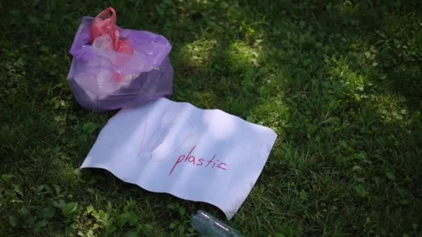 クローズアップ 市立公園の緑の草の上には ゴミが付いているビニール袋 碑文なしのプラスチックおよび空のプラスチックびんが付いているポスターがあります 市立公園でゴミを掃除する — ストック動画