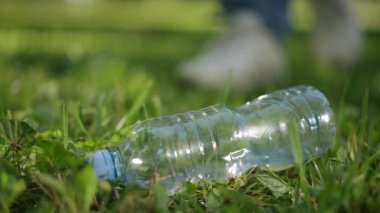 Ağır çekim. Yakın plan. Tanınmayan bir adam çimlerin üzerinde yatan boş bir plastik şişeye yaklaşır ve onu alır. Şehir parkındaki çöpleri temizlemek.