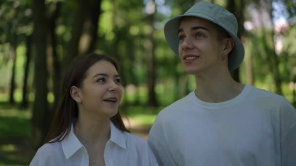 スローモーション 男の子と女の子が屋外で晴れた夏の日に森の中を歩いている 何人かの若者がお互いに話し合い 微笑んでいる — ストック動画