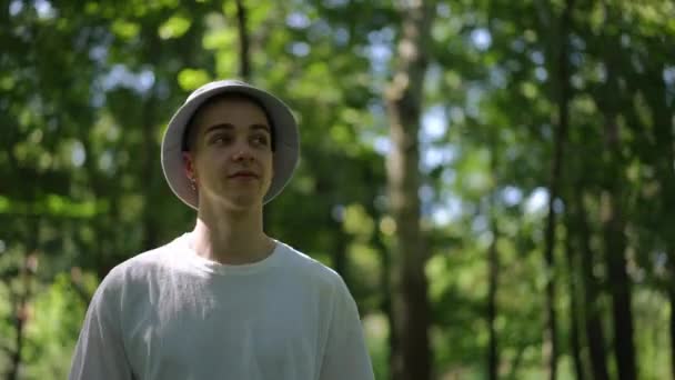 若い男は晴れた夏の日に公園を歩き 彼の頭に太陽の帽子を調整して微笑みます — ストック動画