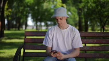 Güneşli bir yaz gününde güneşli bir parkta güneş şapkalı bir adam bankta oturur ve titizlikle elindeki cep telefonunun ekranına bakar. Adam gergin ve etrafa bakıyor.