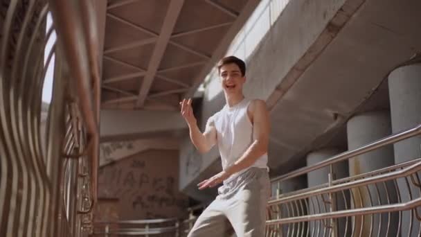低アングルショット スローモーション 若い陽気な男が屋外の橋の下に立って演じるストリートダンス 若い男が踊り 微笑み カメラを見る — ストック動画