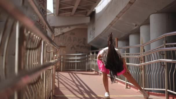 スローモーション サングラスの長い髪を持つ美しい少女は 街の歩行者橋の下でエレガントに踊ります 少女は踊り カメラを見て 彼女の上に腕を上げる — ストック動画