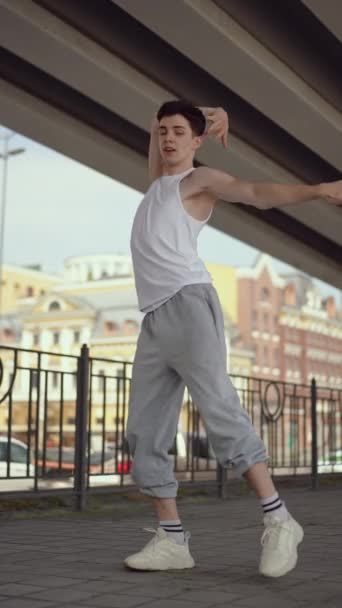 バーティカルビデオ スローモーション ハッピーストリートの男性ダンサーが街の橋の下で屋外で踊っています ストリートダンス中に男は笑って笑う — ストック動画