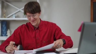 Gözlük takan genç bir adam, açık bir dizüstü bilgisayarla kapalı bir masada otururken, eliyle ağzını kapatarak gülüyor. Adam dizüstü bilgisayarında üzerinde yazılı grafikler olan bir pano gösteriyor.