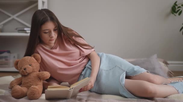 Uma Menina Com Cabelos Longos Está Entusiasticamente Lendo Livro Deitada — Vídeo de Stock