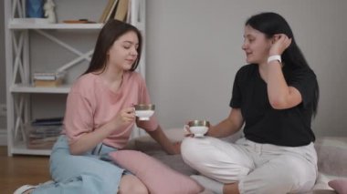 Oturma odasında yerde çay içiyorum. İki kız konuşuyor, gülüyor ve porselen çay fincanlarını ellerinde tutuyorlar modern bir evin odasında battaniyenin üzerinde otururken.