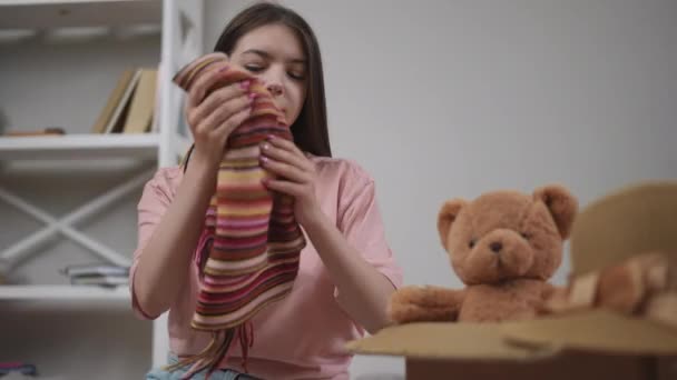 Dziewczyna Wyciąga Pluszowego Misia Wielobarwny Szalik Tekturowego Pudełka Siedząc Podłodze — Wideo stockowe