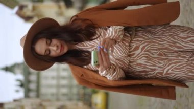 Dikey video. Ağır çekim. Zarif bir kadın şehir caddesinde yürüyor ve bir mesaj geldiğinde cep telefonunun ekranına bakıyor.