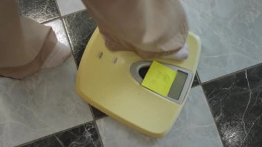 Yakın plan. Geniş pijama pantolonlu tanınmayan bir kız banyo terazisine basıyor ve seramik zemine basıyor. Sağlıklı bir yaşam tarzı için ağırlık kontrolü
