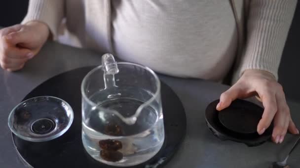 一个无法辨认的孕妇在一个玻璃杯茶壶里煮茶 茶壶盖着一个盖子 酿酒师站在讲台上的桌子上 — 图库视频影像
