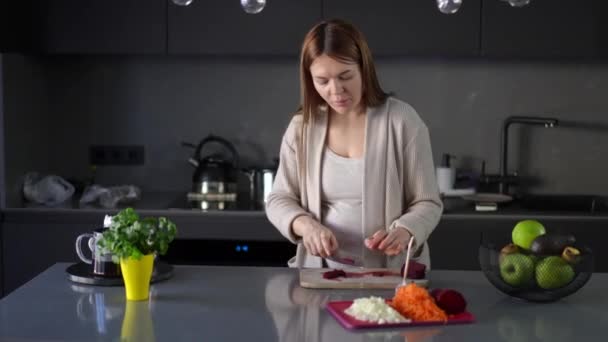 怀孕期间做饭 一个孕妇用菜刀切红色甜菜 一个女人站在厨房桌旁闻大蒜头 感到非常厌恶 — 图库视频影像