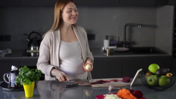 Een Gelukkige Zwangere Vrouw Schilt Uien Met Een Keukenmes Communiceert — Stockvideo