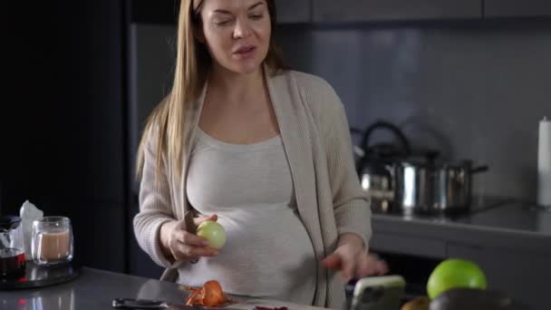 Беременная Женщина Чистит Лук Кухонным Ножом Общается Помощью Мобильного Телефона — стоковое видео