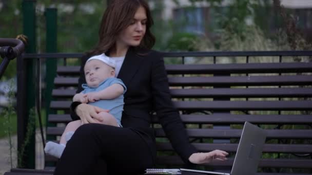 Een Zakenvrouw Werkt Een Laptop Met Een Baby Haar Armen — Stockvideo