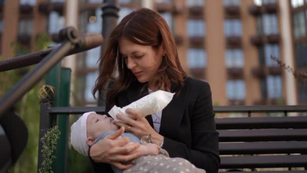 Женщина Кормит Своего Ребенка Бутылки Сидя Скамейке Открытом Воздухе Дворе — стоковое видео