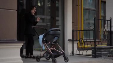 Bir kadın, bebek arabasıyla yürüyüşe çıktı. Bir kadın cep telefonuyla konuşuyor ve bir bebek arabasını caddenin aşağısındaki bir apartmanın bahçesine itiyor.