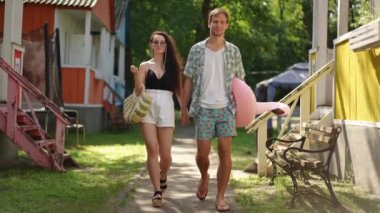 Ağır çekim. Güneşli bir yaz gününde güzel bir çift kumsala gider, dinlenme merkezinin ahşap evleri arasında yürürler.