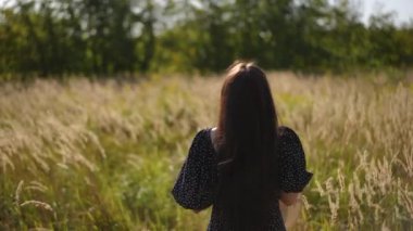 Dikiz aynası. Siyah elbiseli bir kız elinde şapkasıyla kameraya dönük duruyor, açık havada güneşli bir yaz gününde uzun otların arasında. Kız başını çeviriyor.