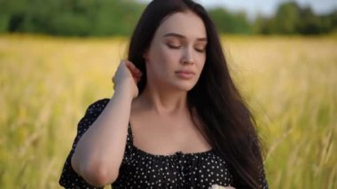 Yakın plan. Uzun saçlı, siyah elbiseli bir kız elinde koparılmış bir kır çiçeğini tutuyor, açık havada güneşli bir yaz gününde uzun çayırların arasında duruyor. İçinde çayır çiçeği olan tatlı bir kız.