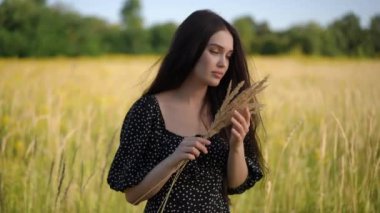 Siyah saçlı esmer bir kız elinde sarı dikenli bir buket tutuyor, açık havada güneşli bir yaz gününde arka planda sarı çayır çimlerinin karşısında duruyor. A