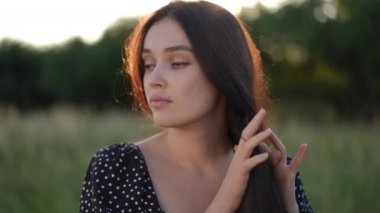 Ağır çekim. Güzel genç bir kadın saçlarını kafasında örüyor ve gün batımında bir yaz tarlasında gülümsüyor.