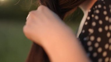 Ağır çekim. Yakın plan. Esmer bir kadın saçını yazın açık havada bir tarlada örüyor.