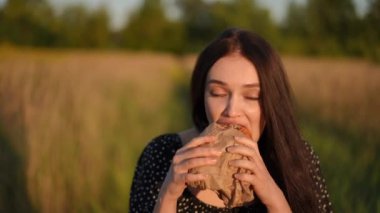 Diş teli takan güzel bir kız gün batımında bir yaz tarlasının ortasında bavulda oturan kocaman bir sandviç yiyor. Kız yiyor, gülümsüyor ve sonra gülmeye başlıyor.
