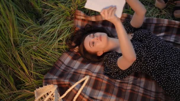 慢动作顶部视图 在一个阳光明媚的夏日 一个女孩躺在田野里 躺在地上看书 黑发姑娘读完这本书后 把它关上 自己按住了 — 图库视频影像