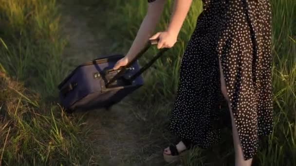 一个女孩把一个带轮子的手提箱上的伸缩手柄折叠起来 日落时分站在夏日的田野上 — 图库视频影像